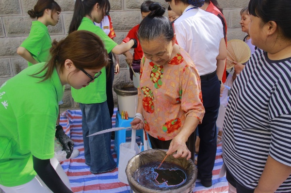 踐行團成員引導(dǎo)居民體驗非遺活動。重慶電力高等?？茖W(xué)校供圖
